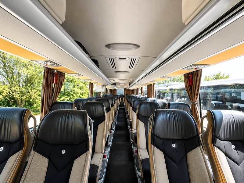 Innenraum des Reisebusses mit dunklen Ledersitzen in Reihen und Mittelgang