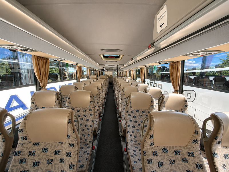 Innenraum des Überlandbusses mit hellen Stoffsitzen und beigen Vorhängen